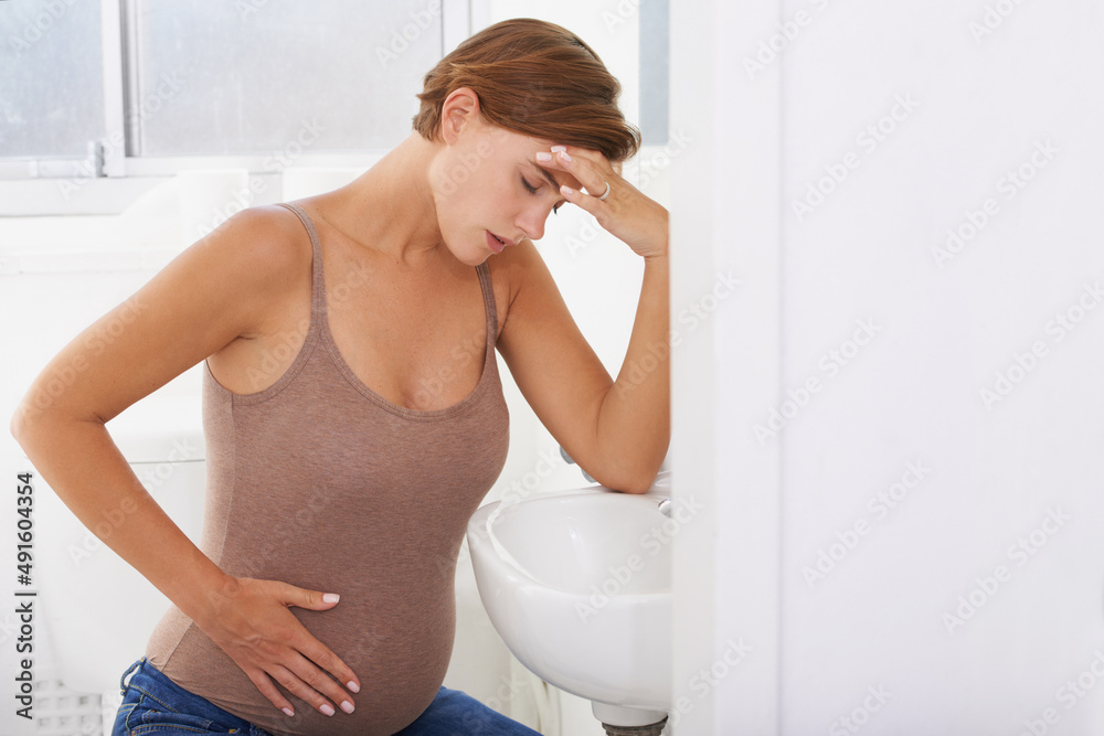 The aches and pains of pregnancy. A pregnant woman struggling with morning sickness in the bathroom. The aches and pains of pregnancy. A pregnant woman struggling with morning sickness in the bathroom.
