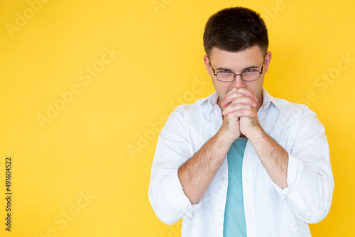 Considering idea. Hopeful man. Faithful believes. Handsome concentrated guy holding hands front of face isolated yellow copy space.
