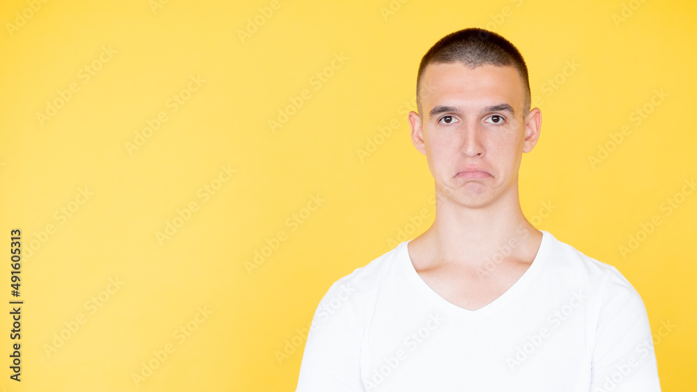 Disappointment regret. Unhappy man. Displeased situation. Upset sorrowful guy in white t-hirt with low edges of lips isolated yellow copy space.