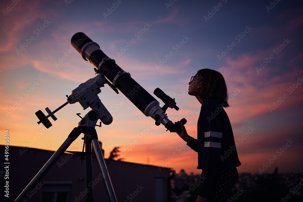 Girl with astronomical telescope stargazing under twilight sky.