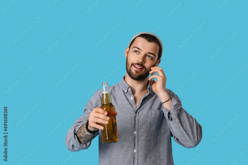 Young bearded man with glass of beer talking by mobile phone on blue background Young bearded man with glass of beer talking by mobile phone on blue background