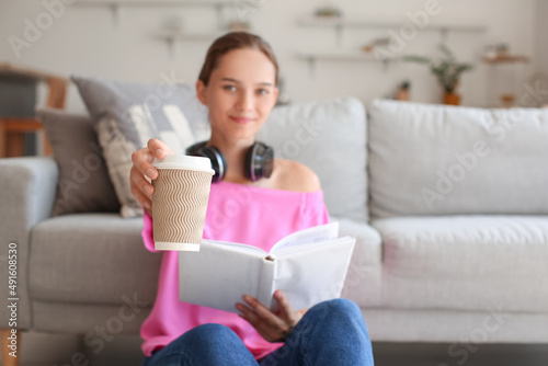 Young woman with book and cup of coffee near sofa at home, closeup