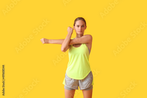 Sporty young woman stretching on yellow background