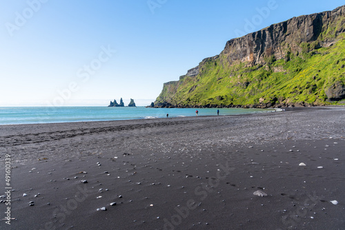 People walking and enjoying themselfs along the shore on a black-sand beach in Iceland. Footprints on the sand are visible in foreground. Vik, Iceland.