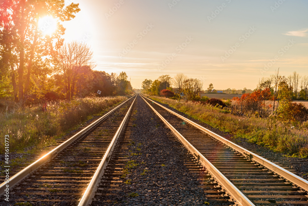 Fototapeta premium Railway tracks running through the countryside at sunset in autumn. Lens flare.