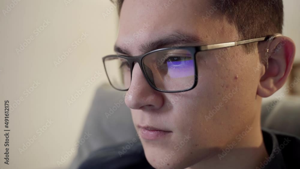 The laptop monitor reflected on the glasses of a young man. Close-up of a focused young businessman. The guy wears computer glasses to reduce eye strain. The laptop monitor reflected on the glasses of a young man. Close-up of a focused young businessman. The guy wears computer glasses to reduce eye strain.