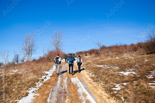 Rear view a group of people hiking on winters trail. Rural road covered by snow. Winter adventure journey. Winter nature landscape. 