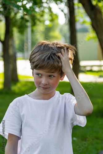 The child scratches his head. A boy with long thick hair has an itchy head due to dandruff.