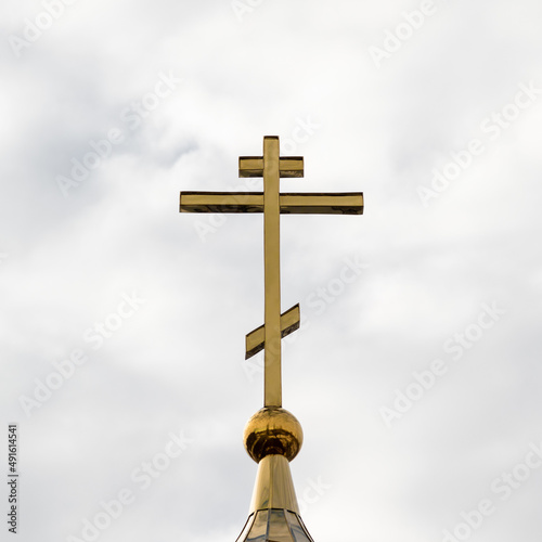 Square photo of an Orthodox cross in cloudy weather against the sky.