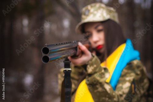 a young girl in military uniform holds a gun in her hands, on her shoulders the flag of Ukraine, aims and shoots, the army defends Ukraine, weapons machine gun, salutes in uniform  photo