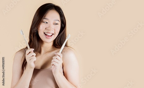 She is holding toothbrush while looking smiling. Asian young woman in studio beige background