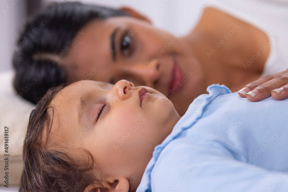 Close-up portrait of sleeping baby and mother lying beside on bed