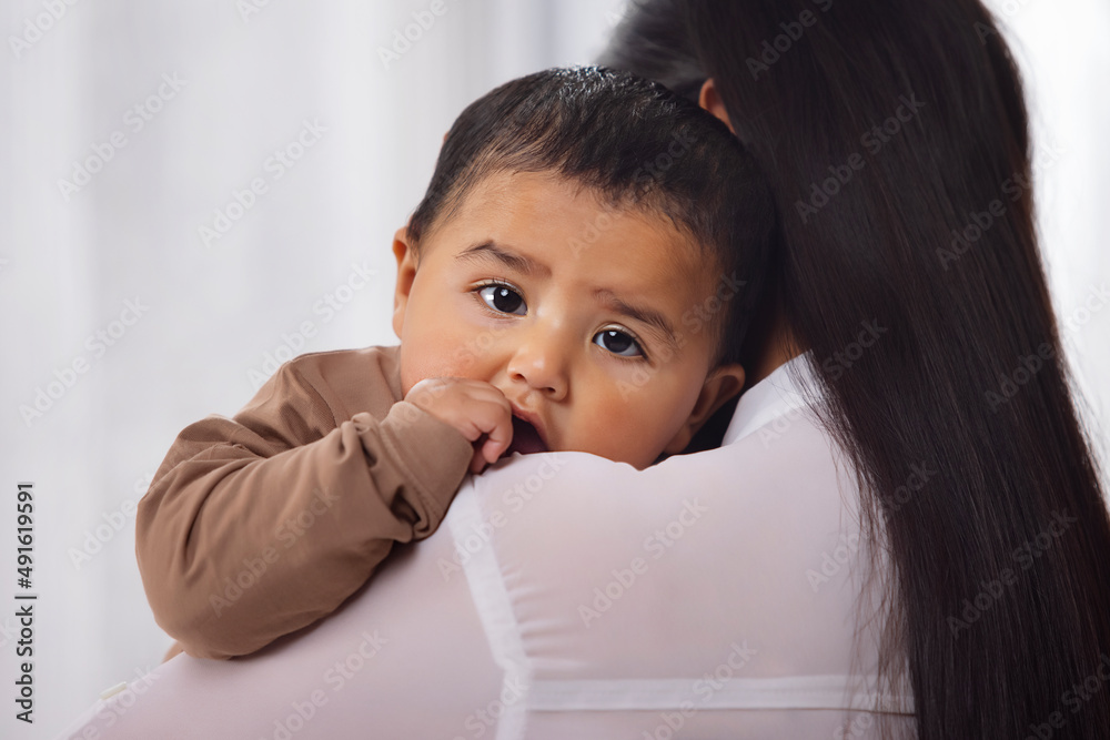 Close-up portrait of a toddler resting on mother's shoulder with thumb in mouth Close-up portrait of a toddler resting on mother's shoulder with thumb in mouth