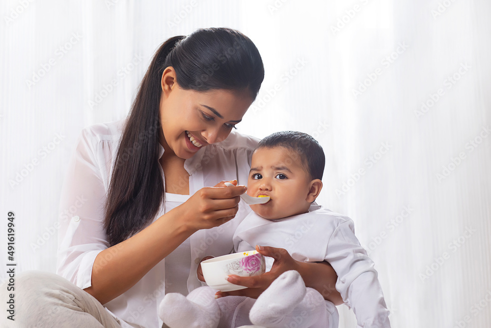 Mother feeding her little baby with spoon at home Mother feeding her little baby with spoon at home