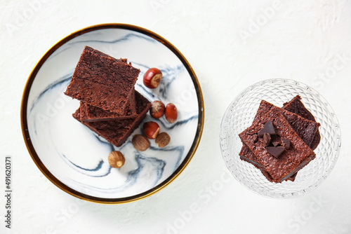 Plate and bowl with pieces of tasty chocolate brownie on light background