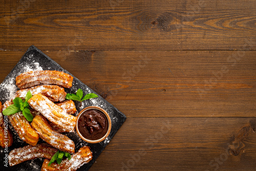 Plate with fried churros and chocolate sauce, top view