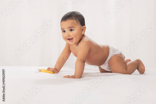 Cute baby in diaper crawling on bed with toy
