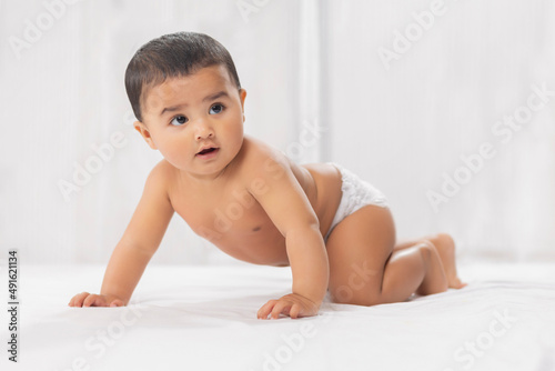 Cute baby in diaper crawling on bed