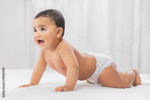 Cute baby in diaper crawling on bed photo