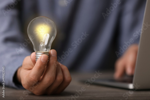 Glow up your ideas. Closeup view of man holding light bulb while working at wooden desk, space for text