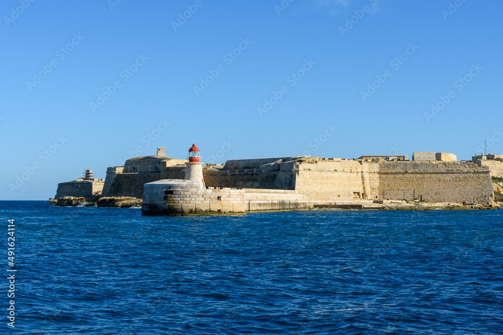 The Ricasoli Breakwater Lighthouse at the entrance to the Grand Harbour. Behind it is Fort Ricasoli - Kalkara, Malta.