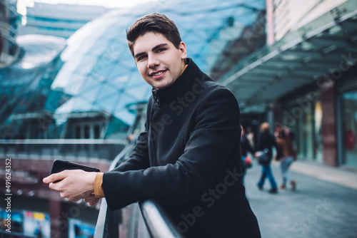 Cheerful man with smartphone standing on street