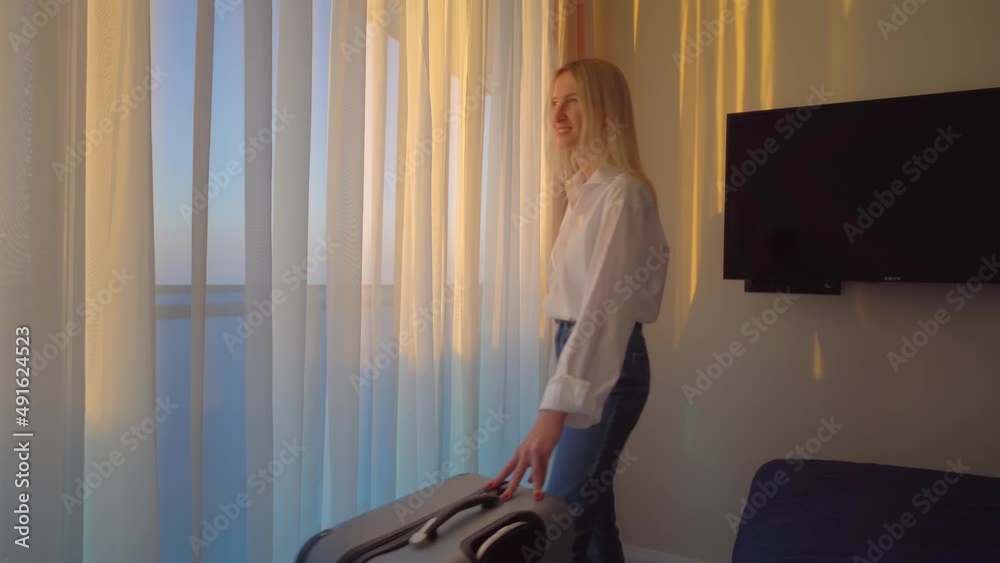 tourists visiting hotel, standing at window and parted curtains, admiring beautiful view with their luggage in hotel bedroom after check-in. concept of travel and recreation. young white woman.