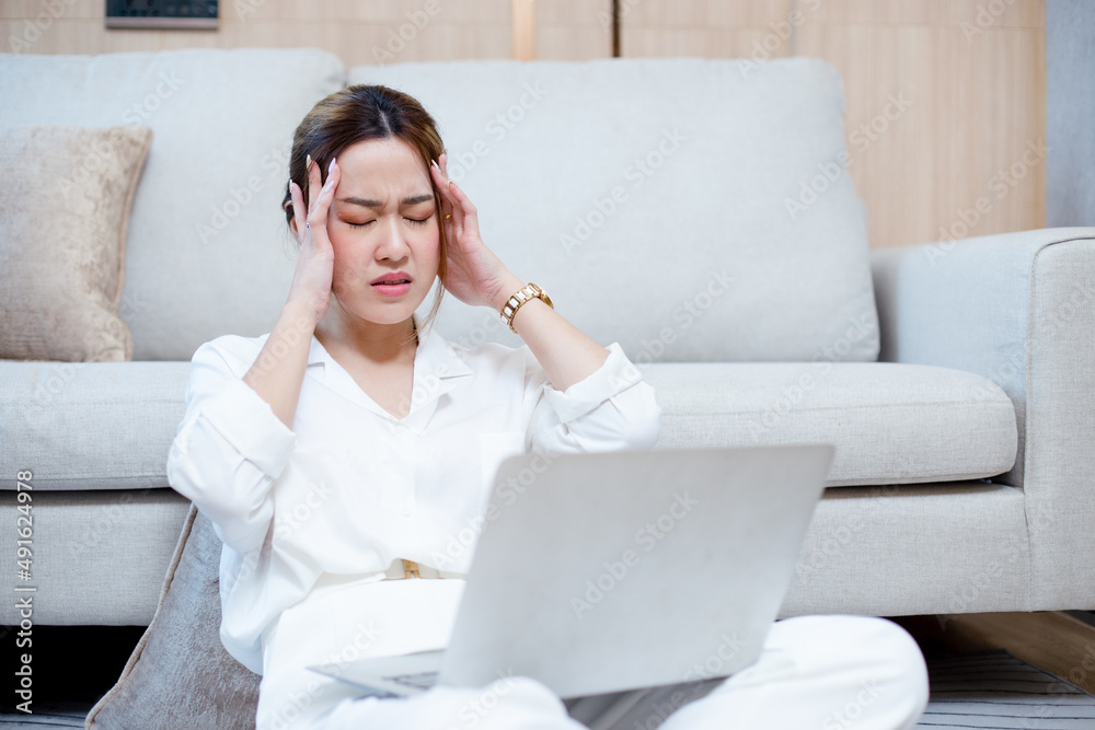 asian woman touching head having a headache working with laptop sitting side sofa in living room home. female office syndrome from overwork. asian woman touching head having a headache working with laptop sitting side sofa in living room home. female office syndrome from overwork.