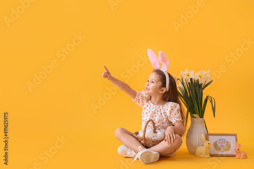Stampa su tela Cute little girl with bunny ears and Easter eggs in basket showing something on