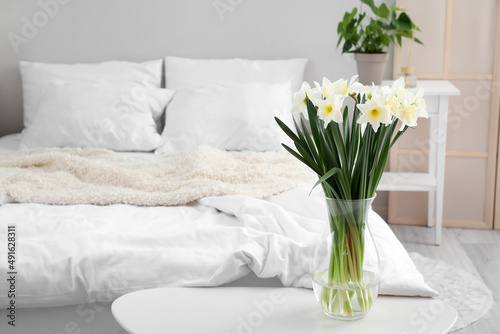Vase with daffodils on table in light bedroom