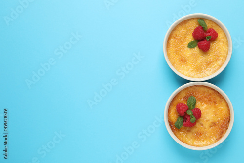 Delicious creme brulee with fresh raspberries in ramekins on light blue background, flat lay. Space for text photo