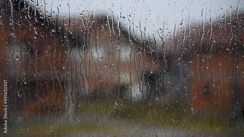 Close up of window pane during rainfall with water streaks and blurred houses in background