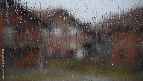 Close up of window pane during rainfall with water streaks and blurred houses in background