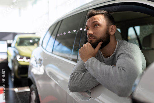a man in a car showroom thinks about buying a new car