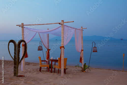 Outdoor cafe romantic table setting on tropical ocean beach at dusk