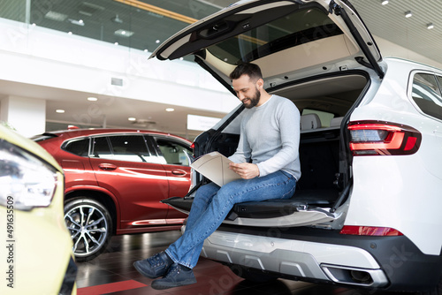 a male buyer in a car dealership flips through a booklet deciding on the purchase of a car