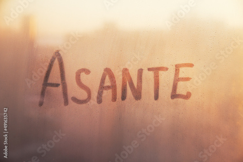 Swahili word Asante thanks in english are painted on wet orange sunrise glass of window photo