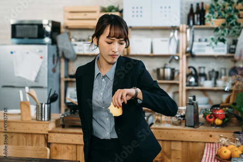 Late for the upcoming meeting, the busy Asian business woman checking the time on watch and have the breakfast rushly late.