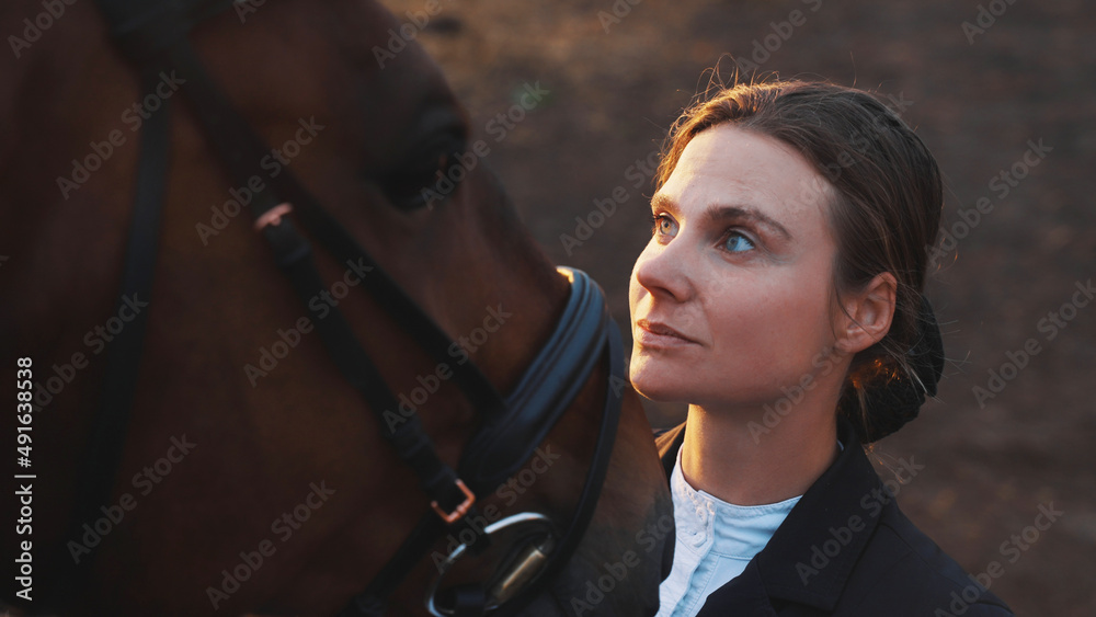 a young beautiful woman from another angle near the horse's head looks at him seriously. High-quality photo