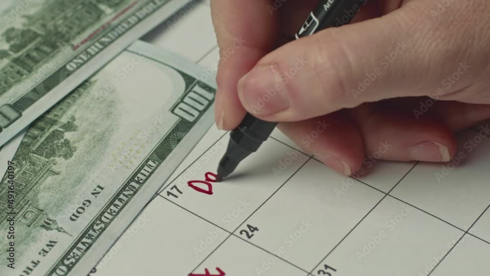 Female hand marking the day in calendar by writing DAY DEBT as a reminder using a red marker. Female hand marking the day in calendar by writing DAY DEBT as a reminder using a red marker.