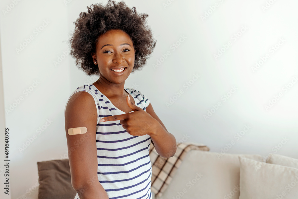 illennial pretty African woman show arm with band aid after vaccination in cozy living room. Protection against covid-19 infection, i got vaccinated, be safety. Vaccination, immunizationconcept. illennial pretty African woman show arm with band aid after vaccination in cozy living room. Protection against covid-19 infection, i got vaccinated, be safety. Vaccination, immunizationconcept.