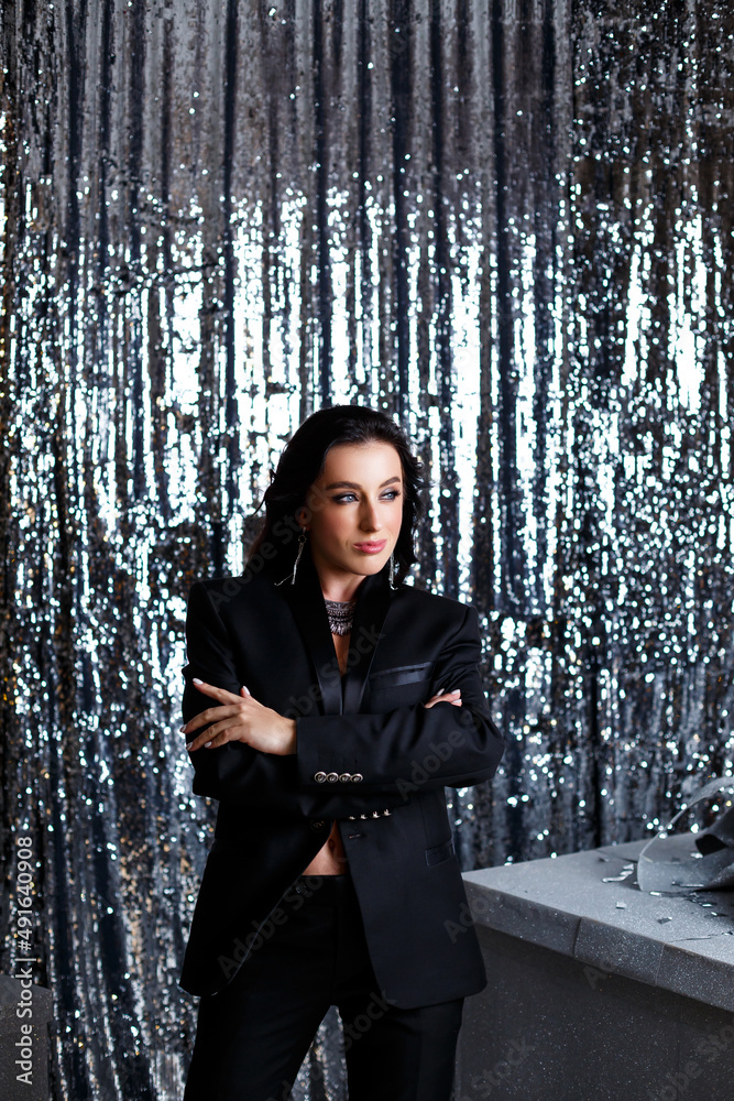 Portrait of a young beautiful woman with dark hair of European appearance. Dressed in a black jacket. Silver shiny background Portrait of a young beautiful woman with dark hair of European appearance. Dressed in a black jacket. Silver shiny background