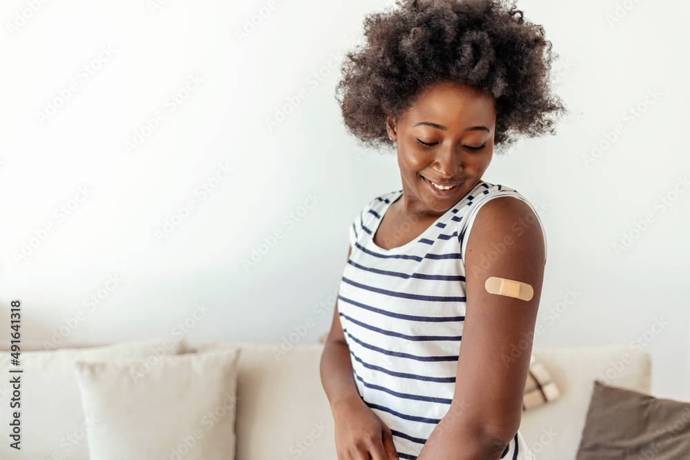 Health care and medical procedure. Smiling millennial beautiful African American lady showing arm with band aid after vaccination in modern home interior. Female get covid-19 immunization at home. Health care and medical procedure. Smiling millennial beautiful African American lady showing arm with band aid after vaccination in modern home interior. Female get covid-19 immunization at home.
