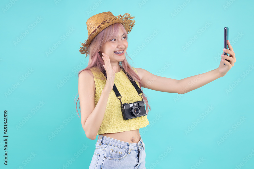 Happy Asian beautiful girl holding a mobile phone on pastel green mint color background. Young traveler taking selfie image with smart phone.