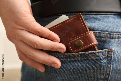 Man putting wallet with money into pocket of jeans, closeup