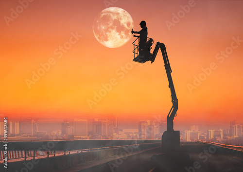 Silhouette of technician working on boom lift to the moon.