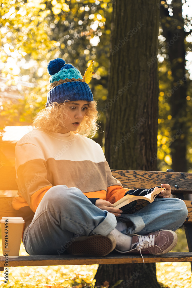 surprised young millennial girl reading book on bench in park - medium shot. High quality photo