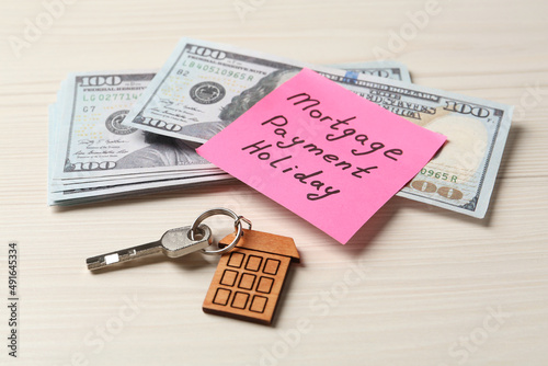 Paper note with words Mortgage Payment Holiday, key and money on white wooden table