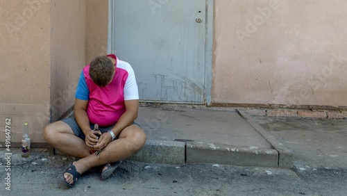 A drunken man sits on the ground. Alcoholism Social problem. The crisis.