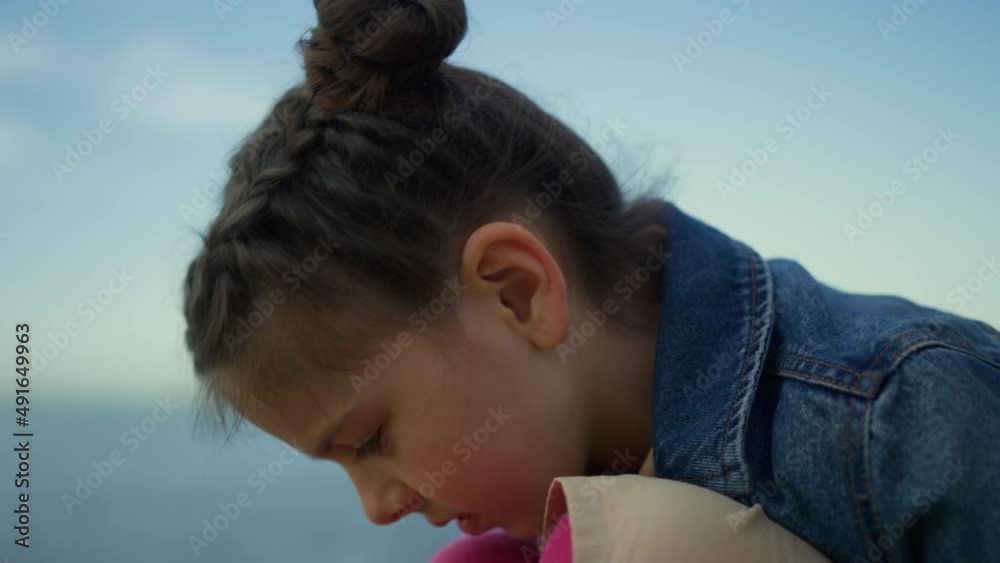 Shy kid sitting beach at sea background. Little girl face looking down on nature Shy kid sitting beach at sea background. Little girl face looking down on nature